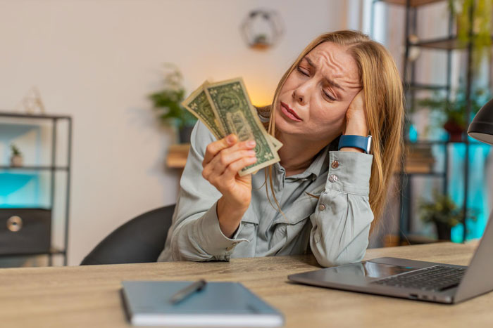 Young woman stressed and holding dollar bills, symbolizing financial and emotional exploitation by manipulative parents.