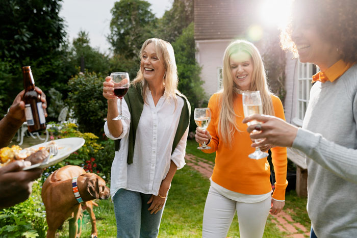 Couple enjoying a garden party outside their big home, smiling and raising glasses in a joyful, kid-free gathering.