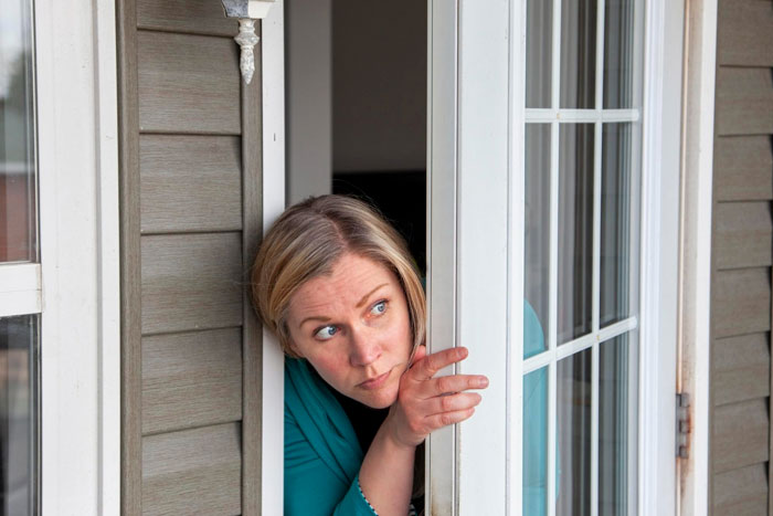 Woman peeking cautiously through a sliding glass door, highlighting neighbor privacy concerns and kids looking through windows. Woman peeking cautiously through a sliding glass door, highlighting neighbor privacy concerns and kids looking through windows.