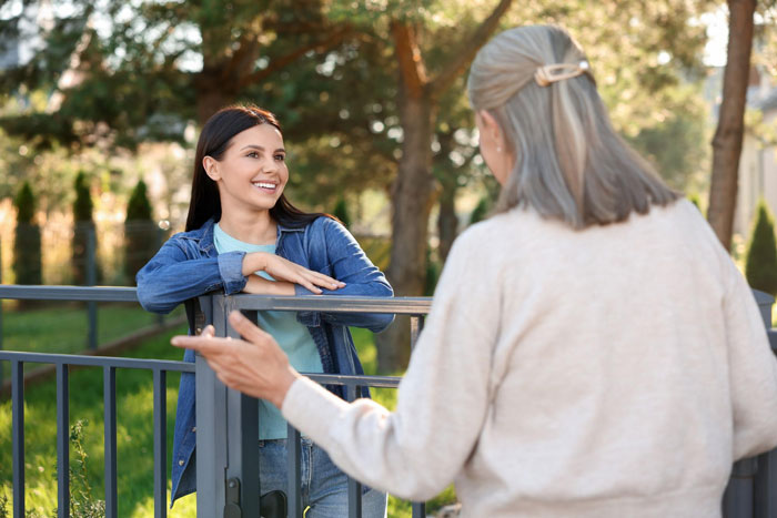 Two women talking over a fence, illustrating a neighbor conflict and threats to report fraud during medical leave.