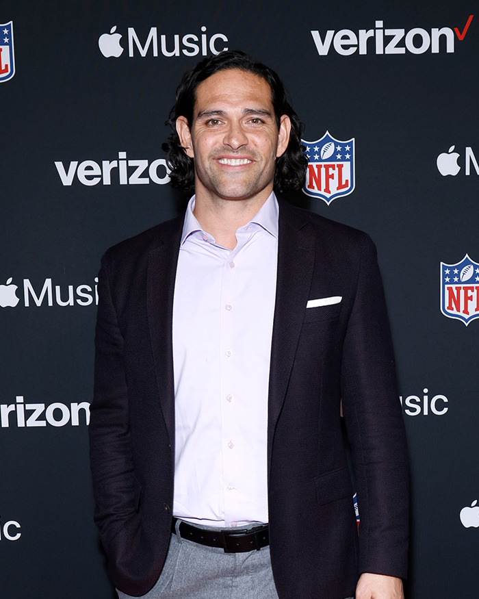 Mark Sanchez at NFL event with Verizon and Apple Music logos in the background, dressed in a blazer and shirt.