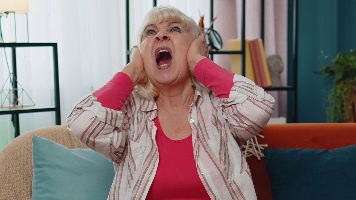 Older woman covering ears and screaming, expressing unhinged behavior in a heated confrontation with new mom at home.
