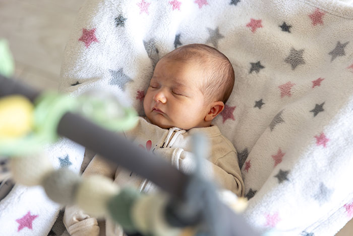 Sleeping baby wrapped in a soft star-patterned blanket highlighting burnt-out wife asking husband to feed the baby.