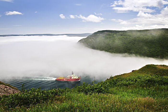 Red ship navigating through dense fog in a scenic valley, illustrating powerful weather records on our planet.