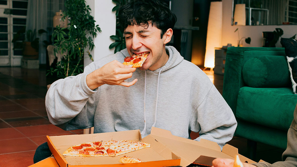 Young man enjoying pizza at home, illustrating common relationship behaviors and red flags women notice after breakups.