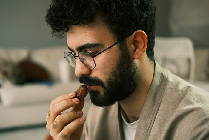 Young man with glasses and beard, deep in thought while holding a small object, reflecting on love and relationships. Young man with glasses and beard, deep in thought while holding a small object, reflecting on love and relationships.