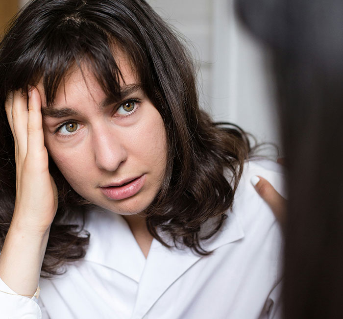 Stressed woman with dark hair holding head, upset during a serious conversation about group activities and neighbors. Stressed woman with dark hair holding head, upset during a serious conversation about group activities and neighbors.