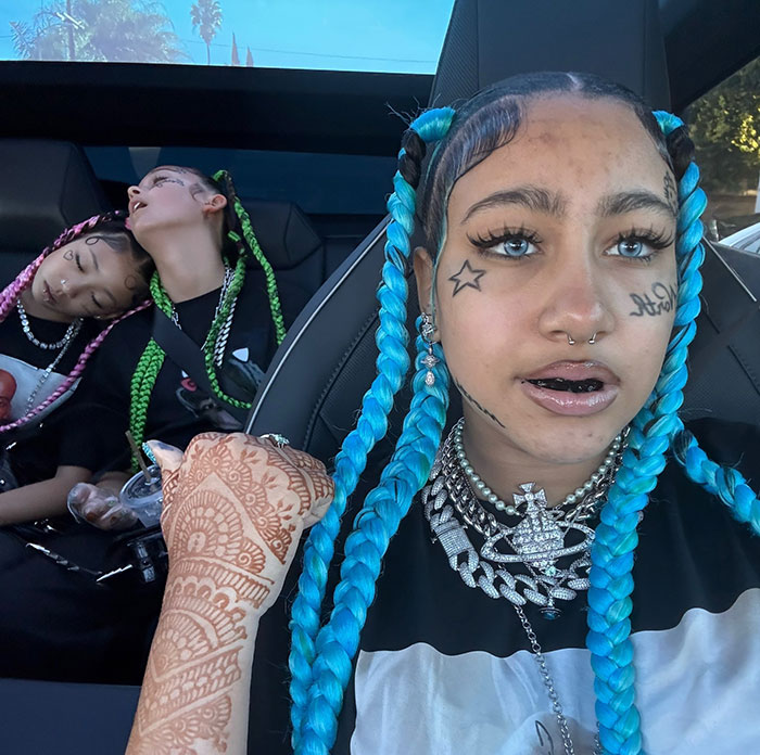 North West with blue braids and facial tattoos sitting in a car, highlighting Kanye West’s warning about her online life. North West with blue braids and facial tattoos sitting in a car, highlighting Kanye West’s warning about her online life.