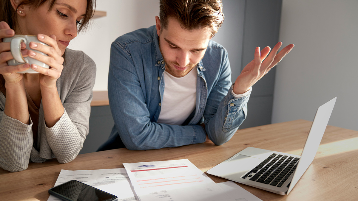 Couple reviewing car accident settlement documents at table while discussing finances with worried expressions.