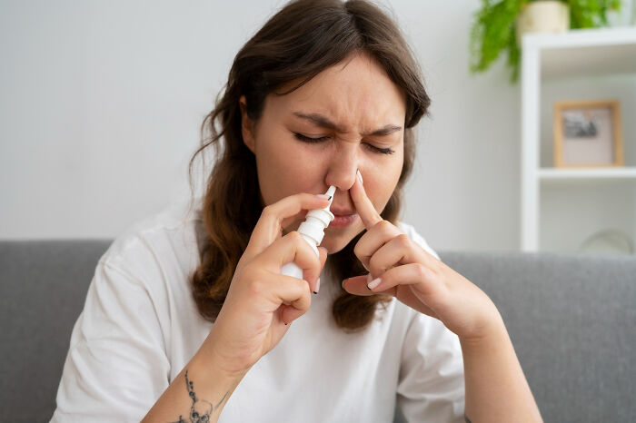 Woman using nasal spray at home with discomfort, illustrating moments patients swore everything was fine but doctors noticed.