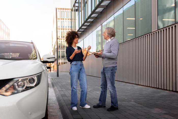 Two people arguing beside a white car in a parking lot outside a modern building, related to daycare manager and car towing.