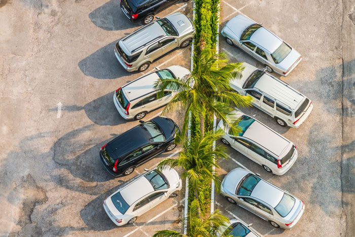 Aerial view of a parking lot with multiple cars parked on both sides of a palm-lined divider in bright daylight. Aerial view of a parking lot with multiple cars parked on both sides of a palm-lined divider in bright daylight.