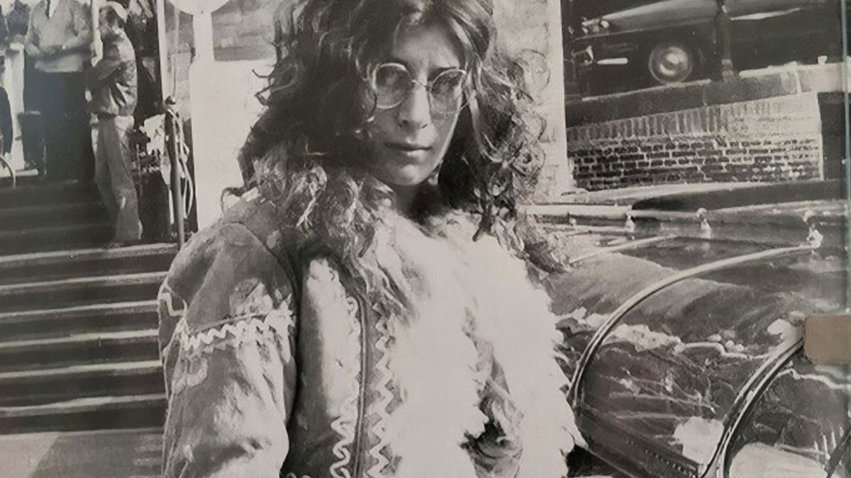 Vintage vacation photo showing a woman with curly hair and glasses in front of a classic car from a time before cell phone cameras.