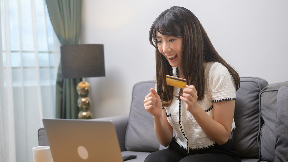 Young woman with credit card excitedly shopping online at home, illustrating misunderstandings about credit card use.