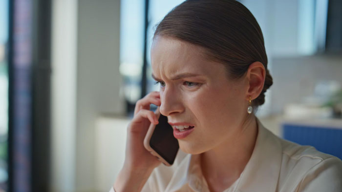 Woman with concerned expression talking on phone indoors, illustrating toxic parents and sibling favoritism issues. Woman with concerned expression talking on phone indoors, illustrating toxic parents and sibling favoritism issues.