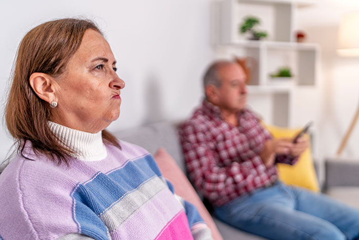 Woman setting a boundary about disabled brother’s care, looking frustrated while man sits on couch using remote control. Woman setting a boundary about disabled brother’s care, looking frustrated while man sits on couch using remote control.
