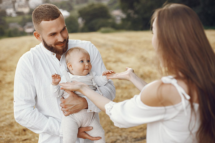 Father holding baby outdoors while wife reaches out, highlighting burnt-out wife and husband feeding baby challenges. Father holding baby outdoors while wife reaches out, highlighting burnt-out wife and husband feeding baby challenges.