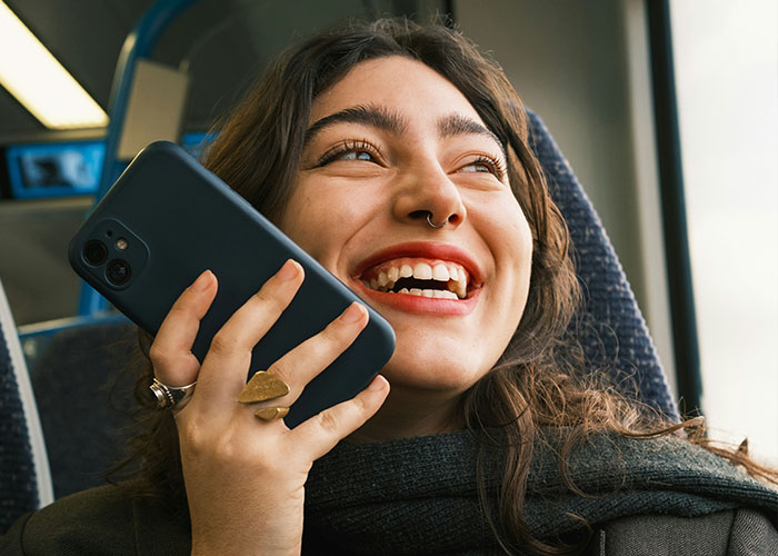 Young woman laughing while holding phone to her ear in a candid moment illustrating shutting down speakerphone users. Young woman laughing while holding phone to her ear in a candid moment illustrating shutting down speakerphone users.