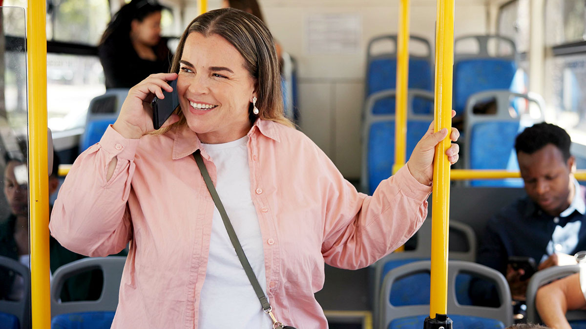 Woman smiling and talking on phone in public transit while holding a pole, illustrating shutting down speakerphone user stories.