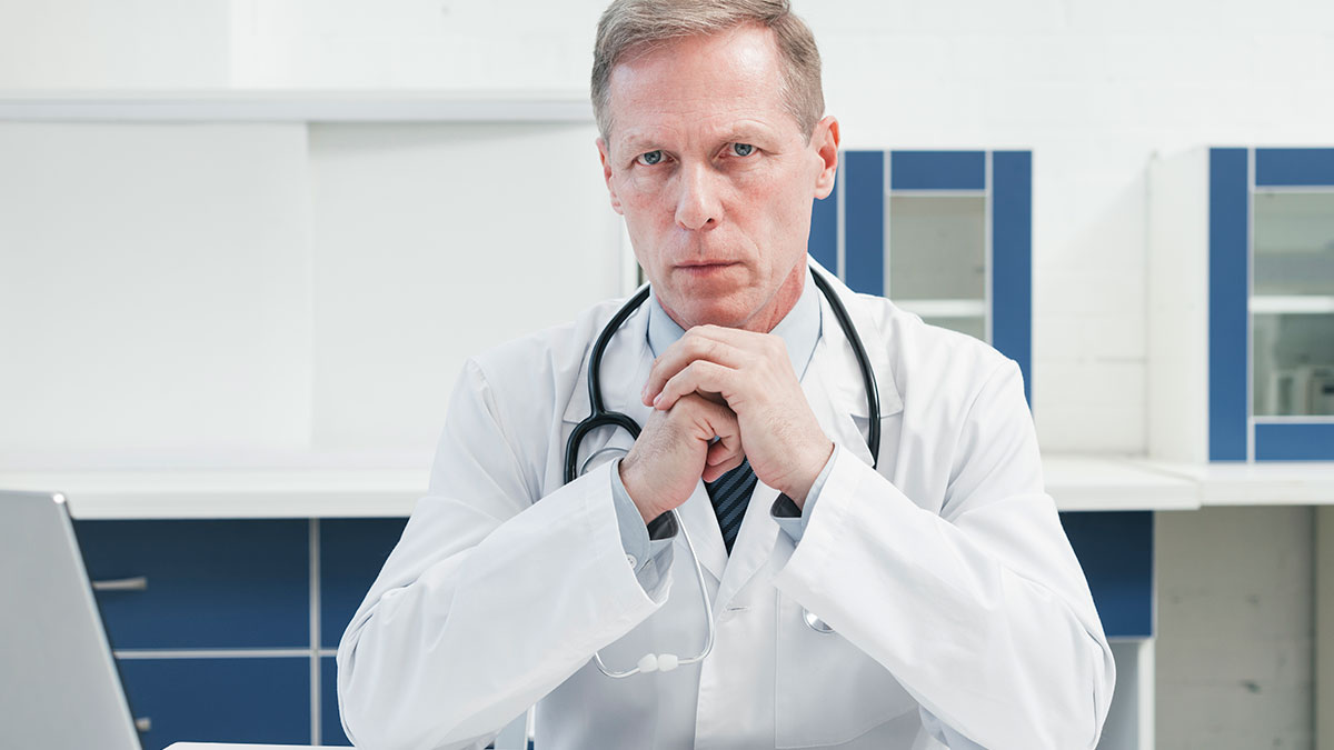 Serious male doctor with stethoscope in a white coat sitting in a medical office sharing health hacks from patients.