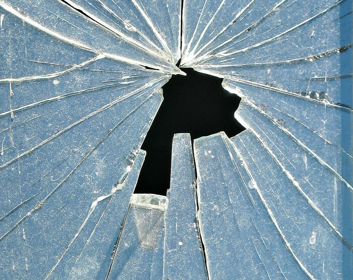 Broken glass window with sharp cracks radiating from a central hole, symbolizing childhood moments people still cringe about.
