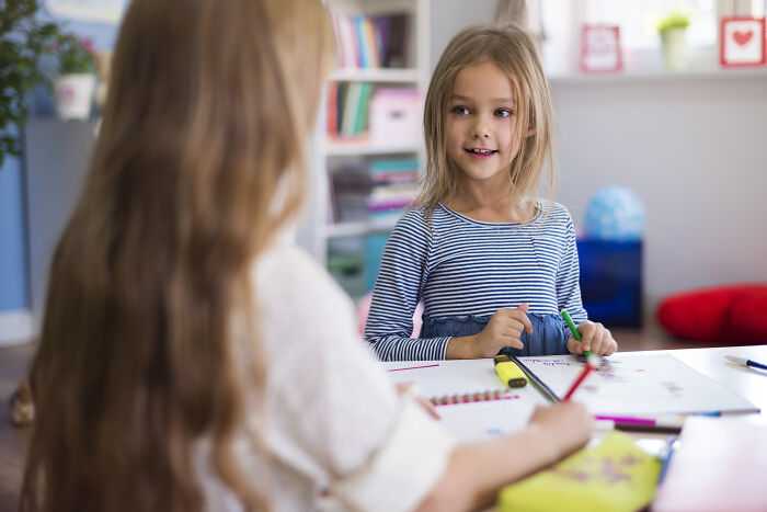 Two young girls drawing and talking at a table, capturing childhood moments people still cringe about today.