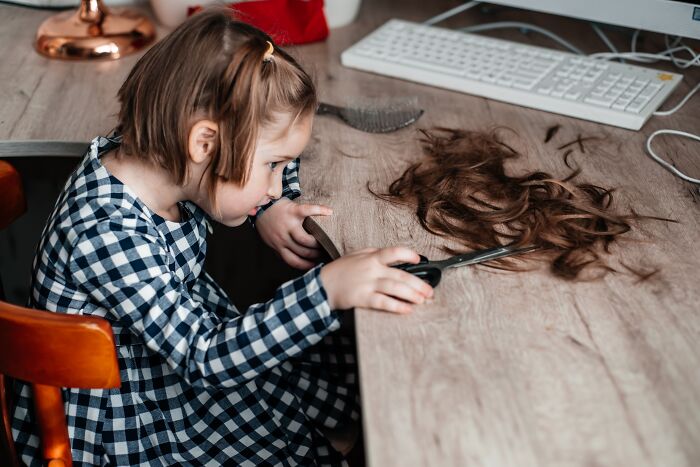 Young girl cutting her own hair at a desk, capturing a childhood moment many still cringe about today.