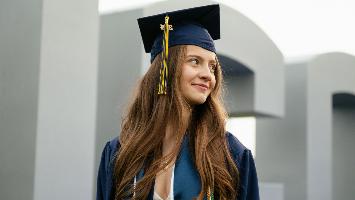 Young woman in graduation cap and gown smiling and looking away, representing people revealing longest grudges held.