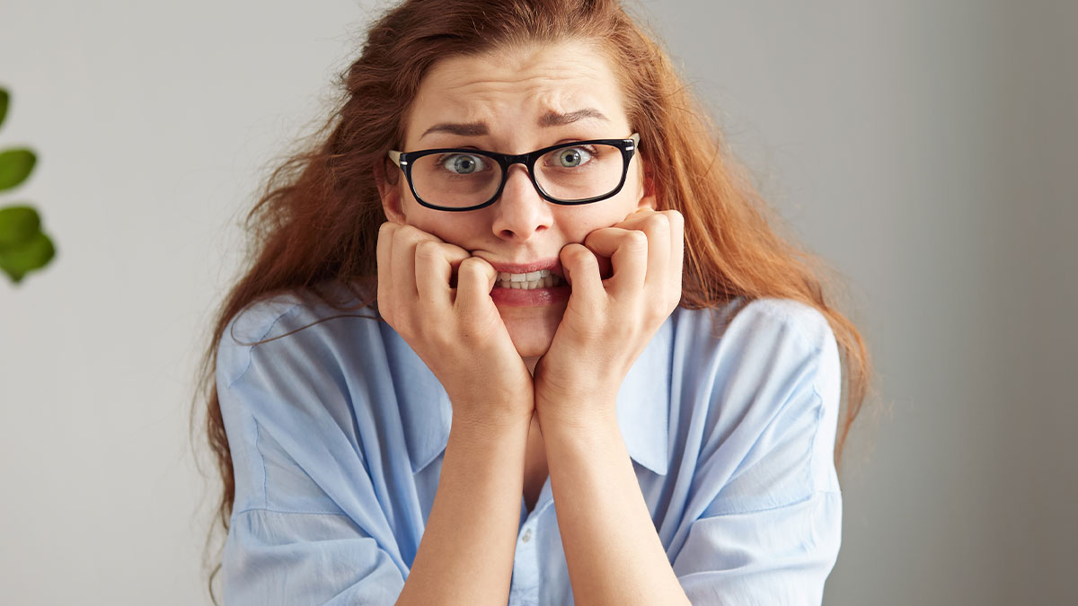 Anxious woman with glasses biting her nails, expressing fear and stress after an unexpected and awkward moment.