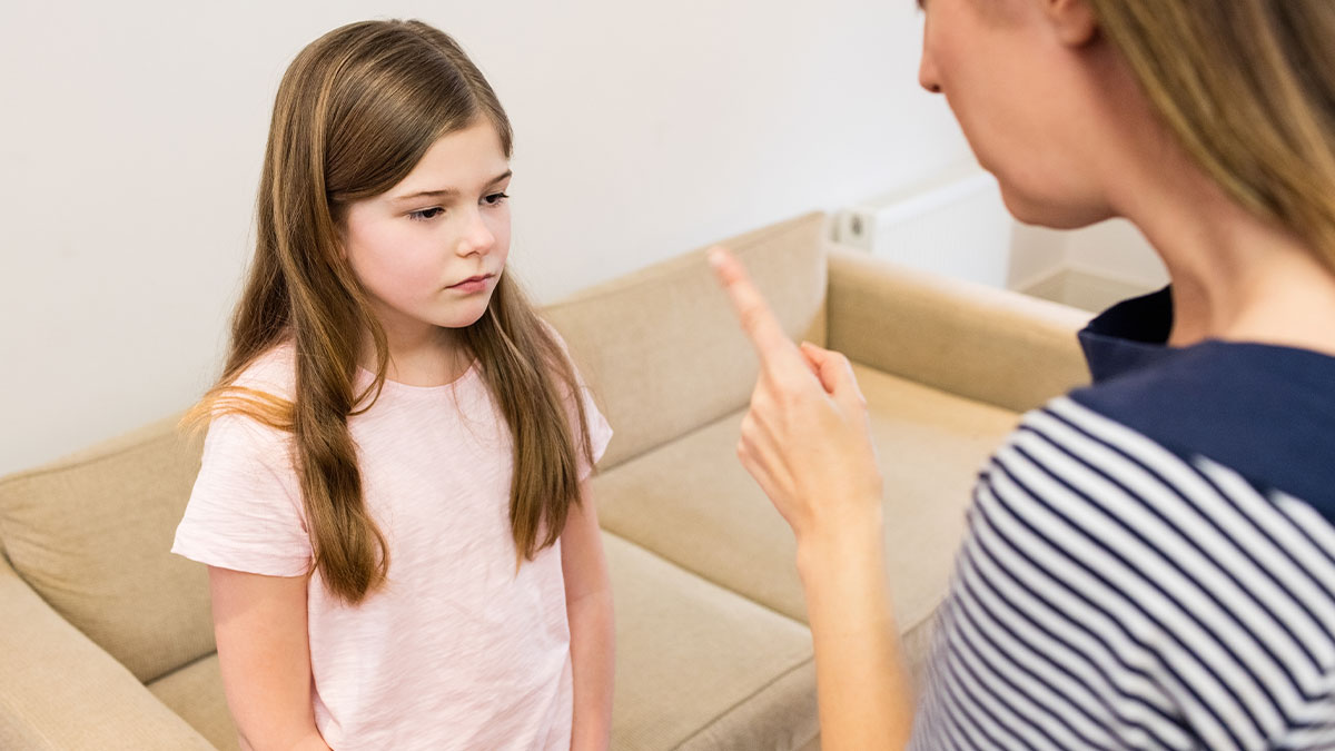 Young girl listening with a sad expression as her mother angrily points a finger during a tense confrontation at home.