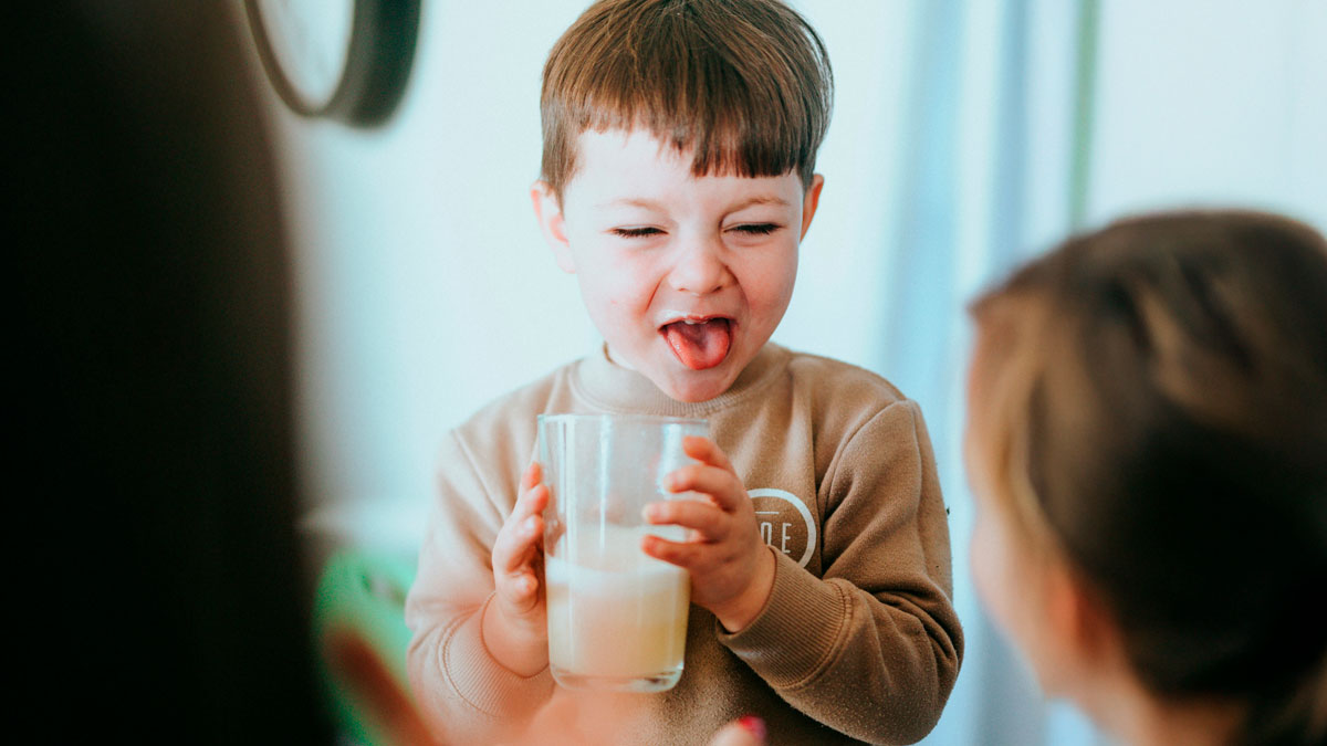 Childhood moment of a young boy making a funny face while holding a glass of milk, capturing playful childhood rules.