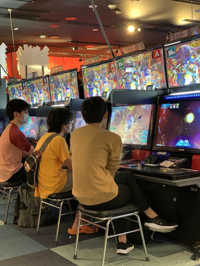 Three people playing arcade games in an arcade, showcasing positive stereotypes of gaming culture in various countries.