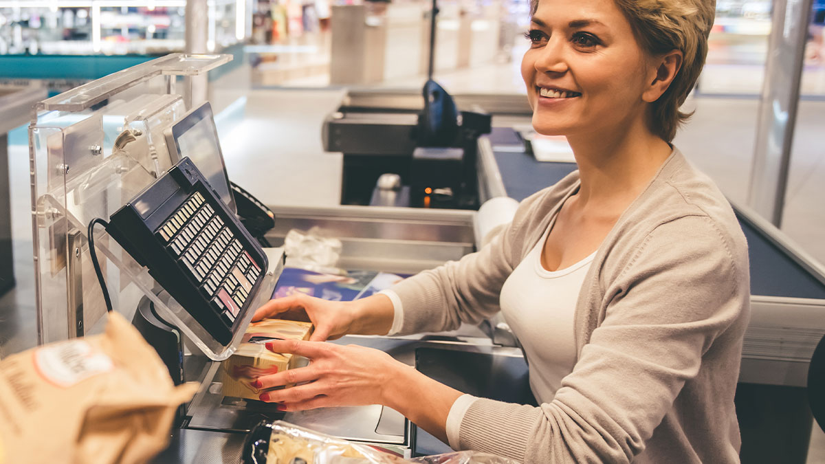 Woman smiling while working as a cashier packing groceries, depicting real and sobering stories about how to ruin your entire life.