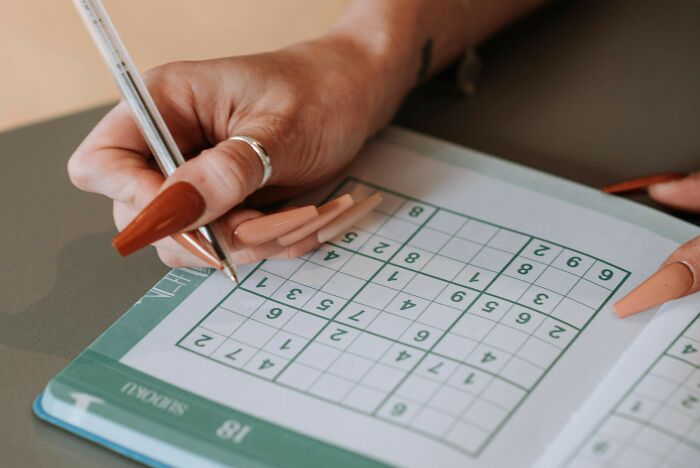 Person solving a sudoku puzzle in a book, focusing on filling numbers in challenging brain-racking sudoku grids. Person solving a sudoku puzzle in a book, focusing on filling numbers in challenging brain-racking sudoku grids.