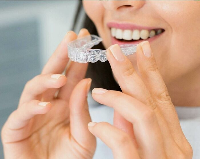 Woman smiling while holding a clear dental retainer close to her mouth, illustrating first signs that scream someone is having an affair.