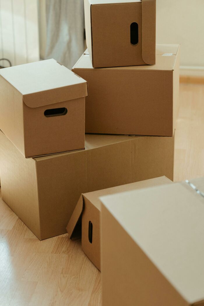 Stack of plain cardboard boxes on wooden floor inside a home, illustrating weird things workers have seen inside strangers’ homes.