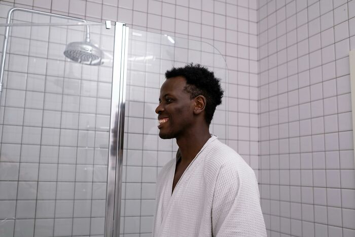 Man smiling in a white robe standing in a tiled bathroom with a glass shower door, illustrating disturbing things folks were told.