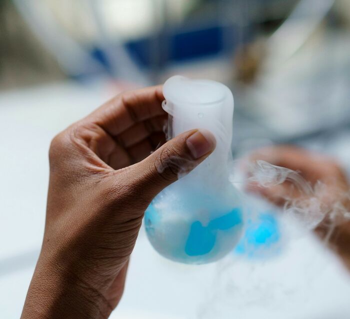 Hand holding a laboratory flask with blue liquid and smoke, illustrating people share potentially dangerous situations.