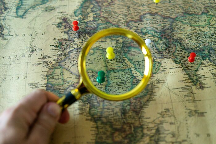 Magnifying glass focusing on Africa with colorful pins on a vintage map for geography expert challenge. Magnifying glass focusing on Africa with colorful pins on a vintage map for geography expert challenge.