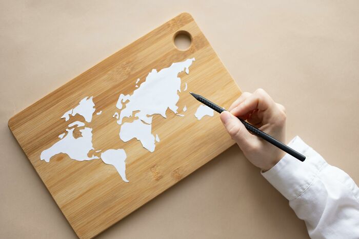Hand holding pen near world map on wooden board representing visual geography quiz concept. Hand holding pen near world map on wooden board representing visual geography quiz concept.