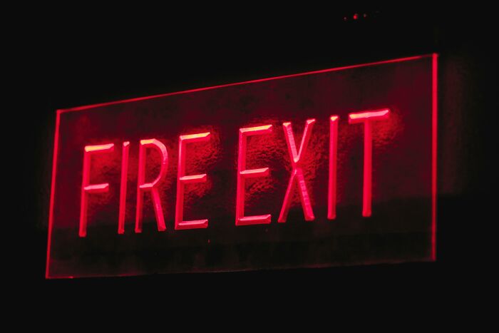 Red neon fire exit sign glowing against a dark background representing potentially dangerous situations.