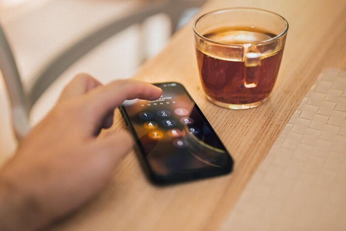 Hand holding smartphone entering passcode next to glass of tea, illustrating first signs that scream someone is having an affair.
