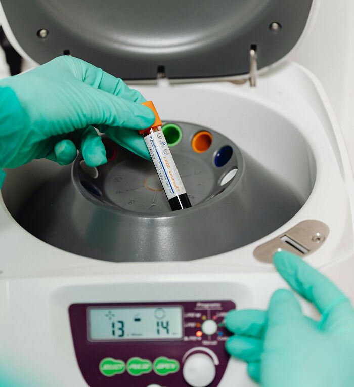 Gloved hands placing a blood sample into a centrifuge, highlighting people share potentially dangerous situations in labs.