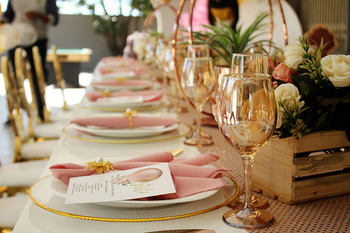 Elaborate wedding table setting with pink napkins, floral centerpieces, and elegant glassware in a bright venue. Elaborate wedding table setting with pink napkins, floral centerpieces, and elegant glassware in a bright venue.