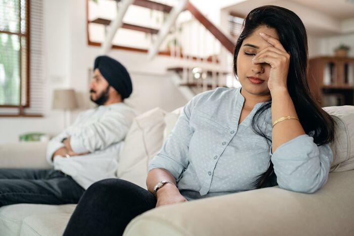 Couple sitting apart on a couch showing signs of tension and distress indicating potential affair signs and relationship issues.