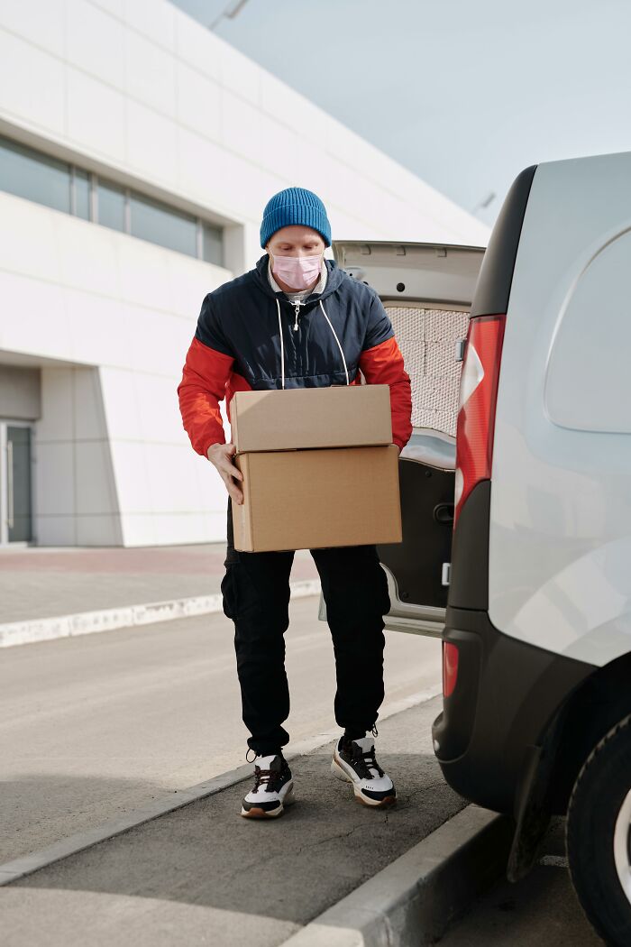 Delivery worker wearing a mask carrying boxes from a van, illustrating workers seeing weird things inside strangers’ homes.