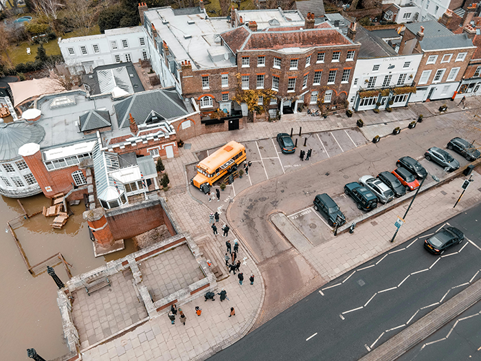 Aerial view of a group near a yellow school bus by historic buildings, emphasizing mom expected to put autistic student's needs first. Aerial view of a group near a yellow school bus by historic buildings, emphasizing mom expected to put autistic student's needs first.