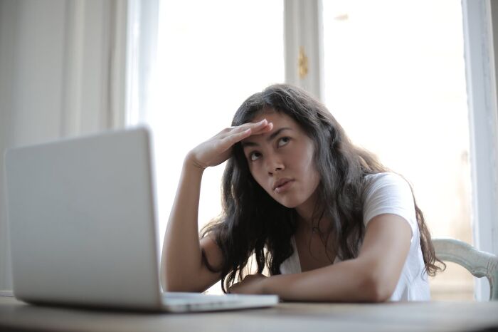 Young woman looking stressed and thoughtful while sitting at a table with a laptop, reflecting signs someone is having an affair.