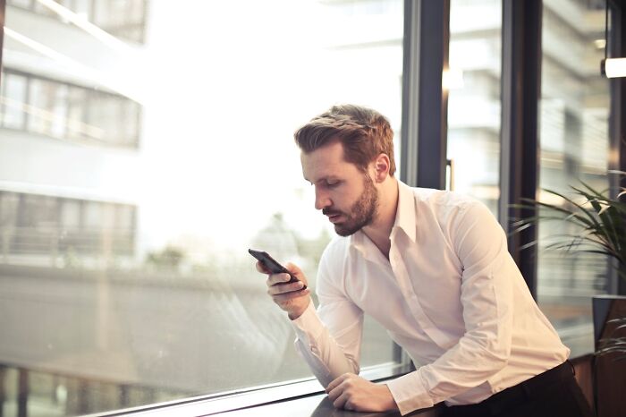 Man in a white shirt looking intently at his phone, possibly showing signs that scream someone is having an affair.