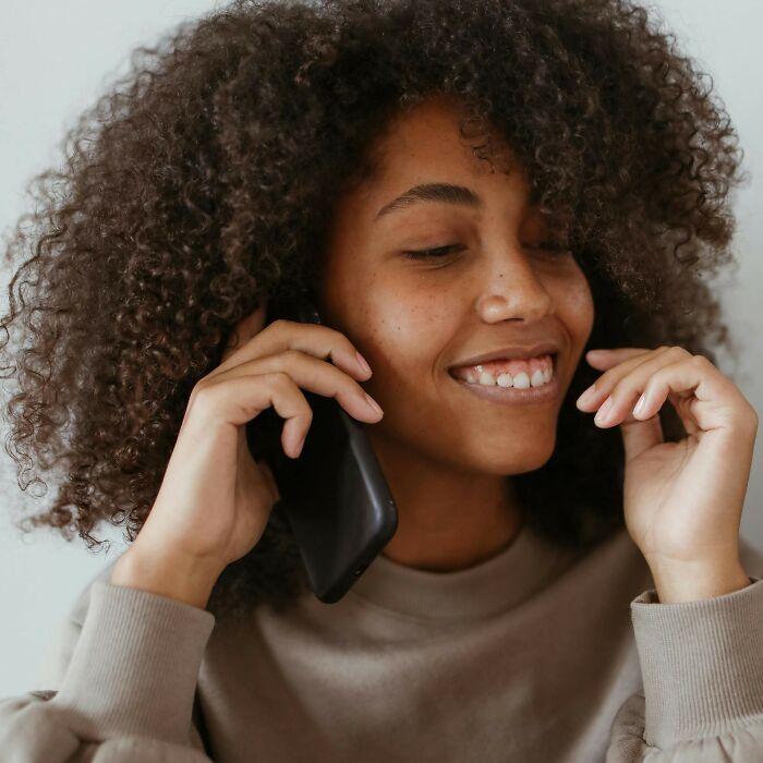 Woman with curly hair smiling while talking on a phone, illustrating disturbing things folks were told and later found creepy.
